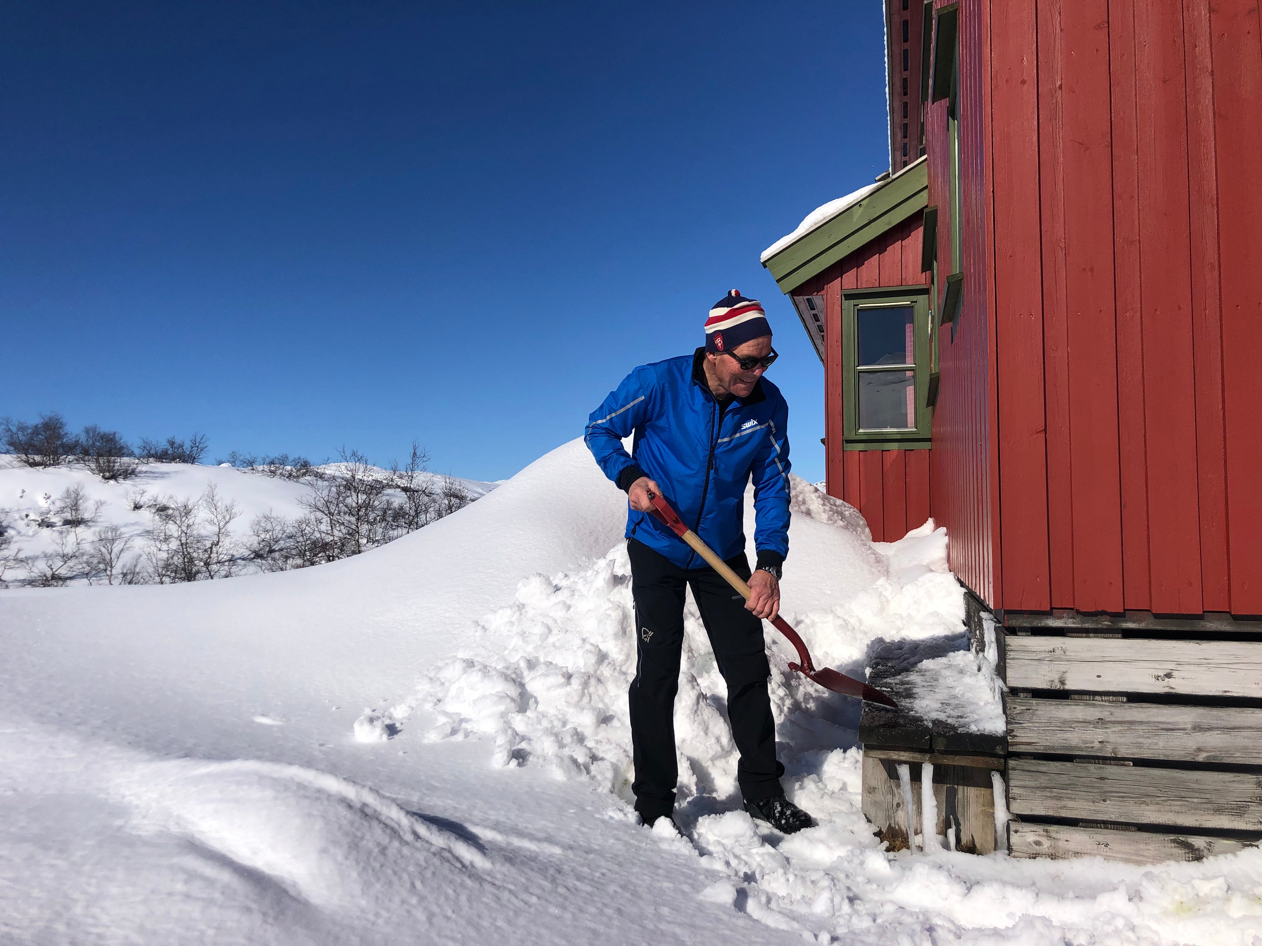 Mann m&aring;ker sn&oslash; utenfor r&oslash;d hytte