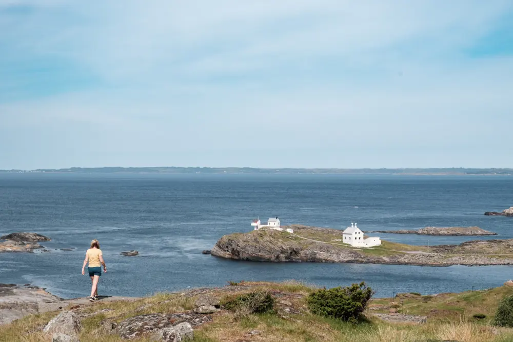 En kvinne går ute i naturen mot et fyr i havgapet.