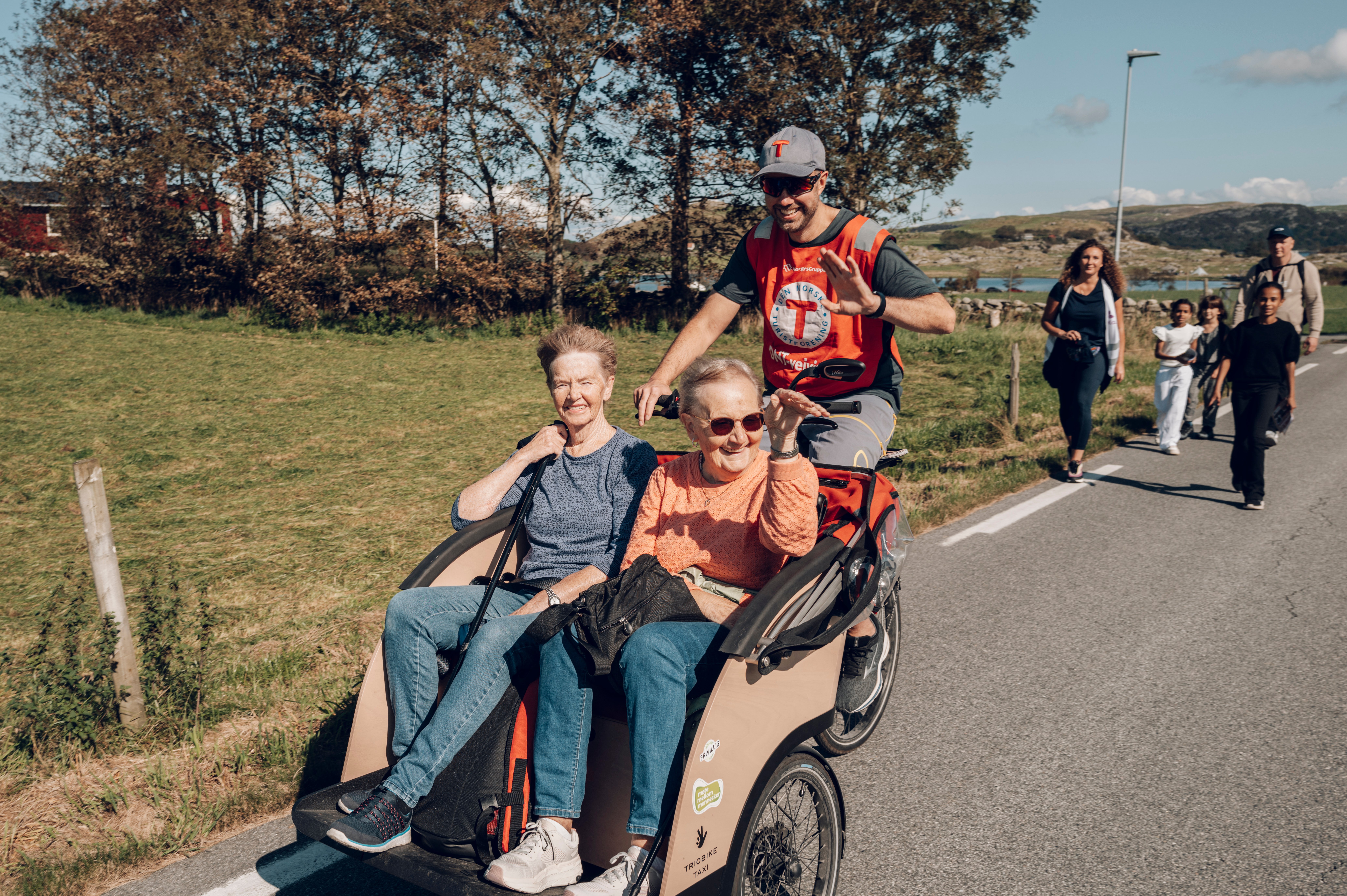 Mann sykler to damer i transportsykkel p&aring; vei i naturen