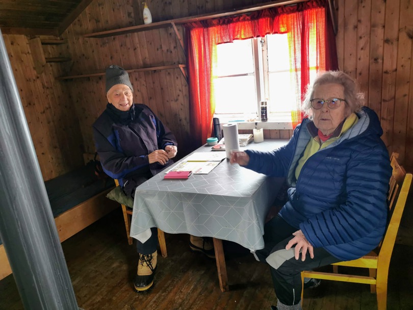 To eldre personer koser seg inne på koia.
