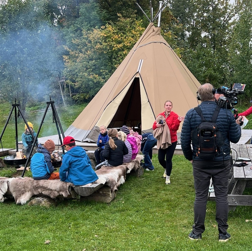 Barn som sitter ved bålpanner foran Lavvo