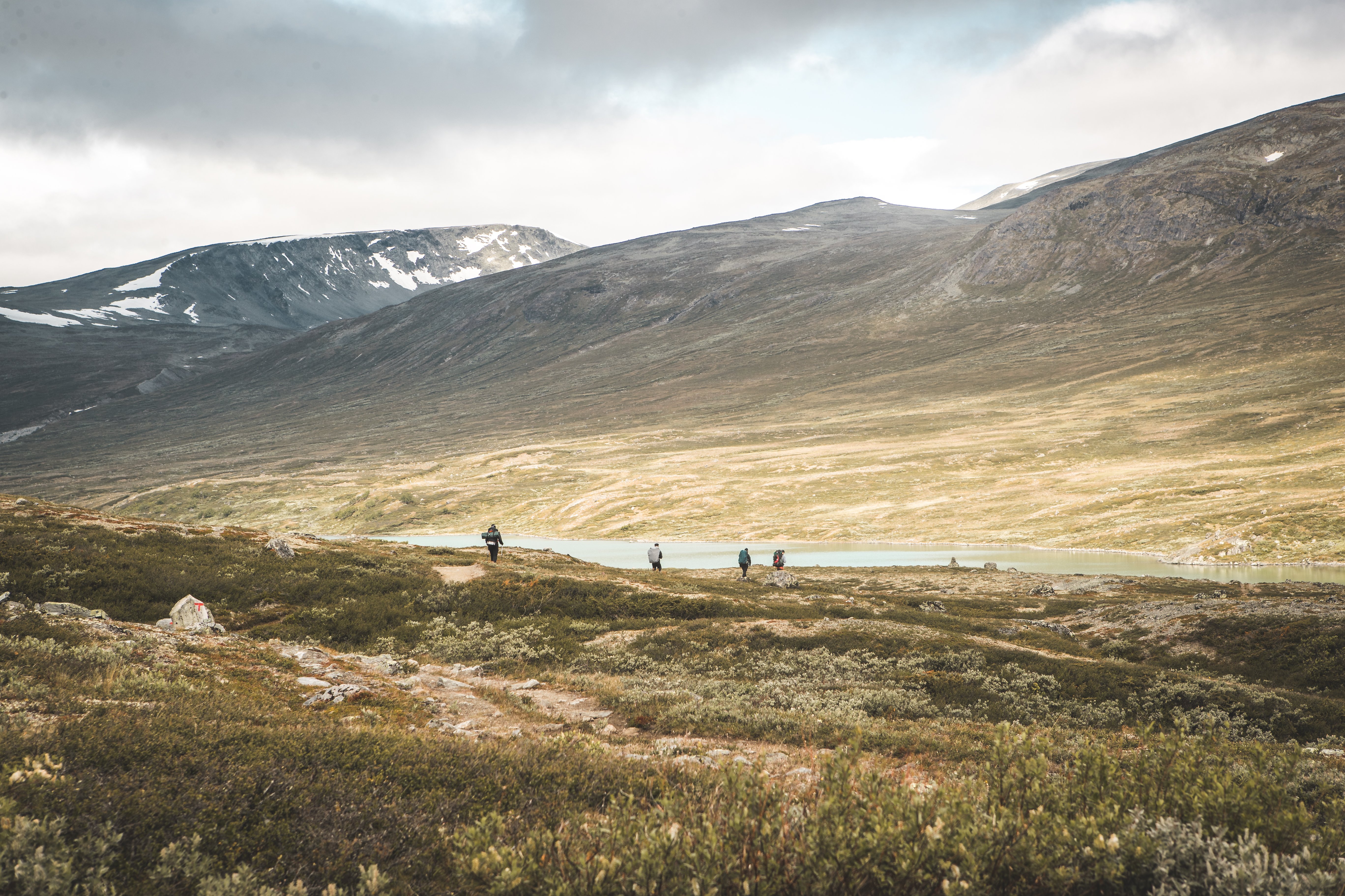 Fjell på høsten med et vann og fire personer i forgrunnen.