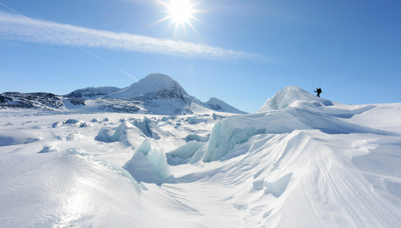 Skiløper skimtes blant snø- og isformasjoner på en isbre ved et fjell. 