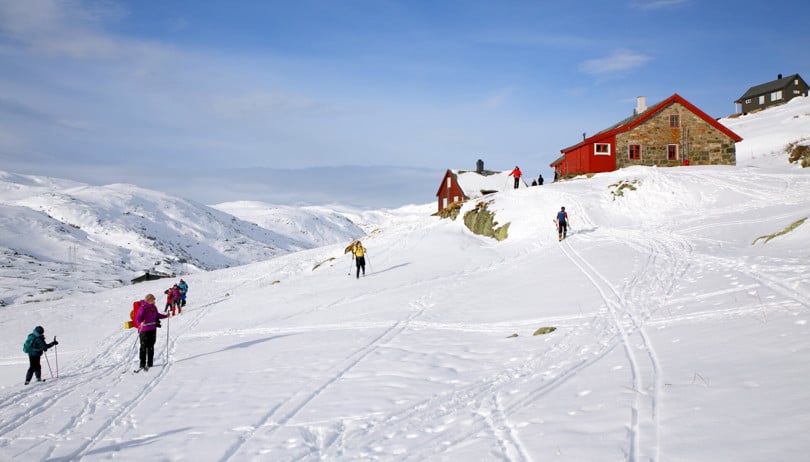Flere skiløpere på vei mot ei steinhytte på fjellet. 