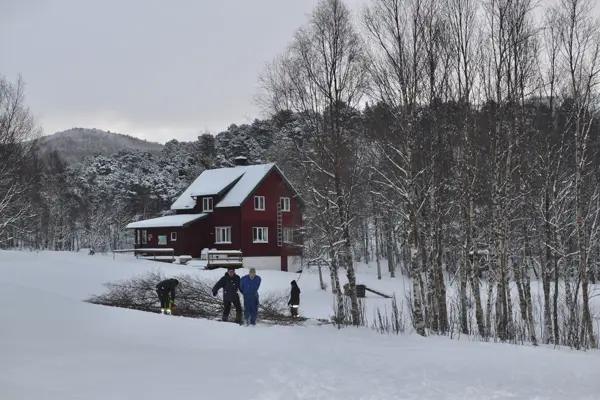 Folk som trekker på vedkvister foran et hus 