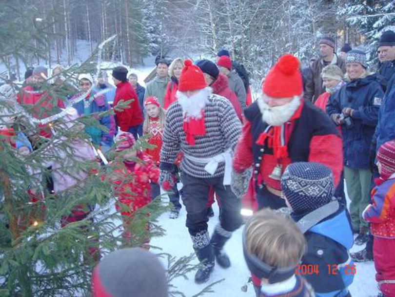 Mange barn, voksene og julenissen som går rundt juletreet