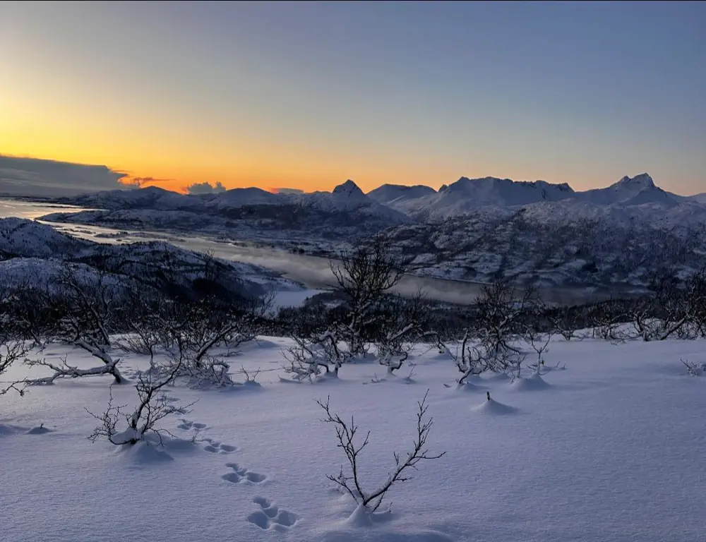 Sol under horisont bak snødekte fjell