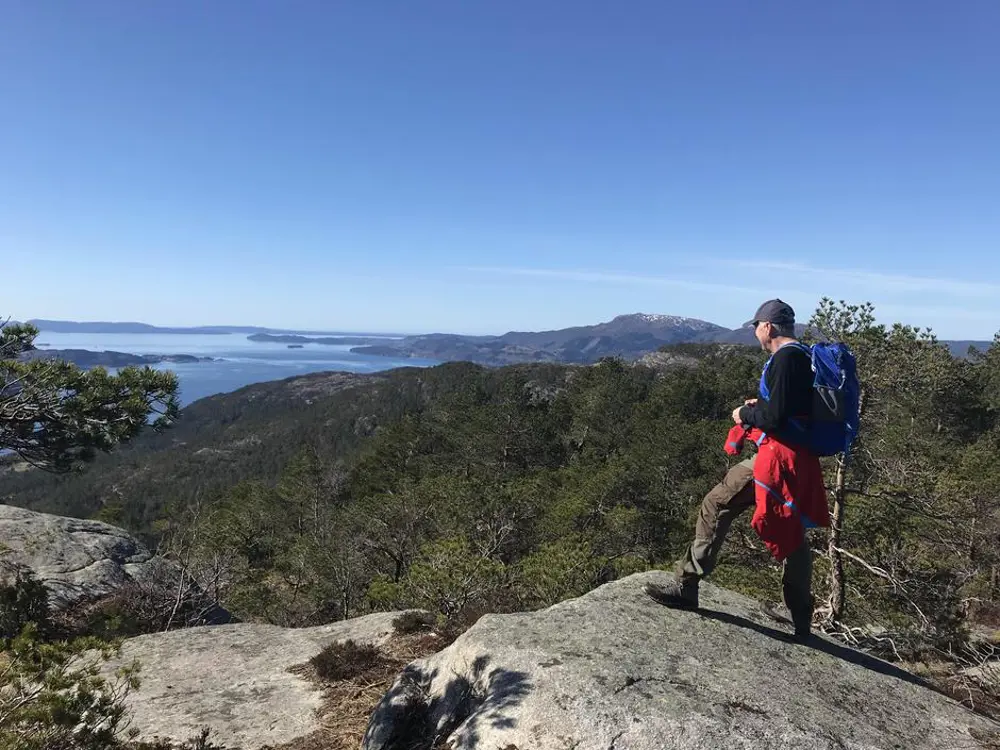 Ein turgåar på toppen av eit fjell med utsikt mot fjord og andre fjell og toppar i sol og blå himmel