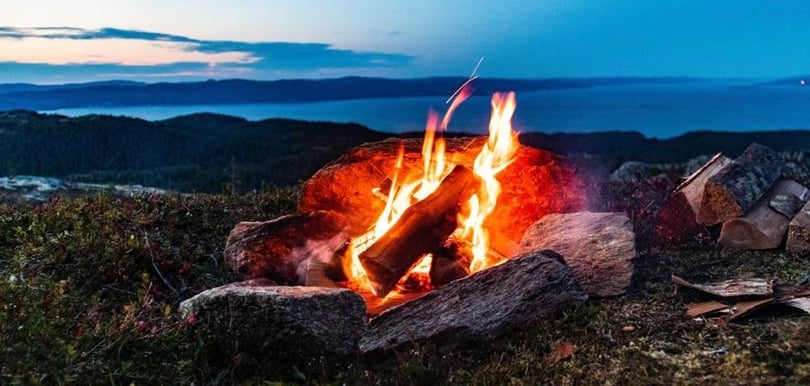 Bildet viser et leirbål på en topp med utsikt over havet.