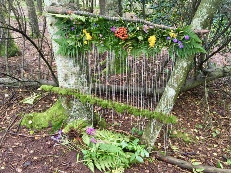 Tråder er hengt opp mellom to trær og pyntet med diverse blader og blomster fra naturen.