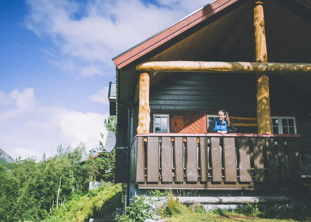 dame står på terrasse i fjellhytte omringet av grønne omgivelser