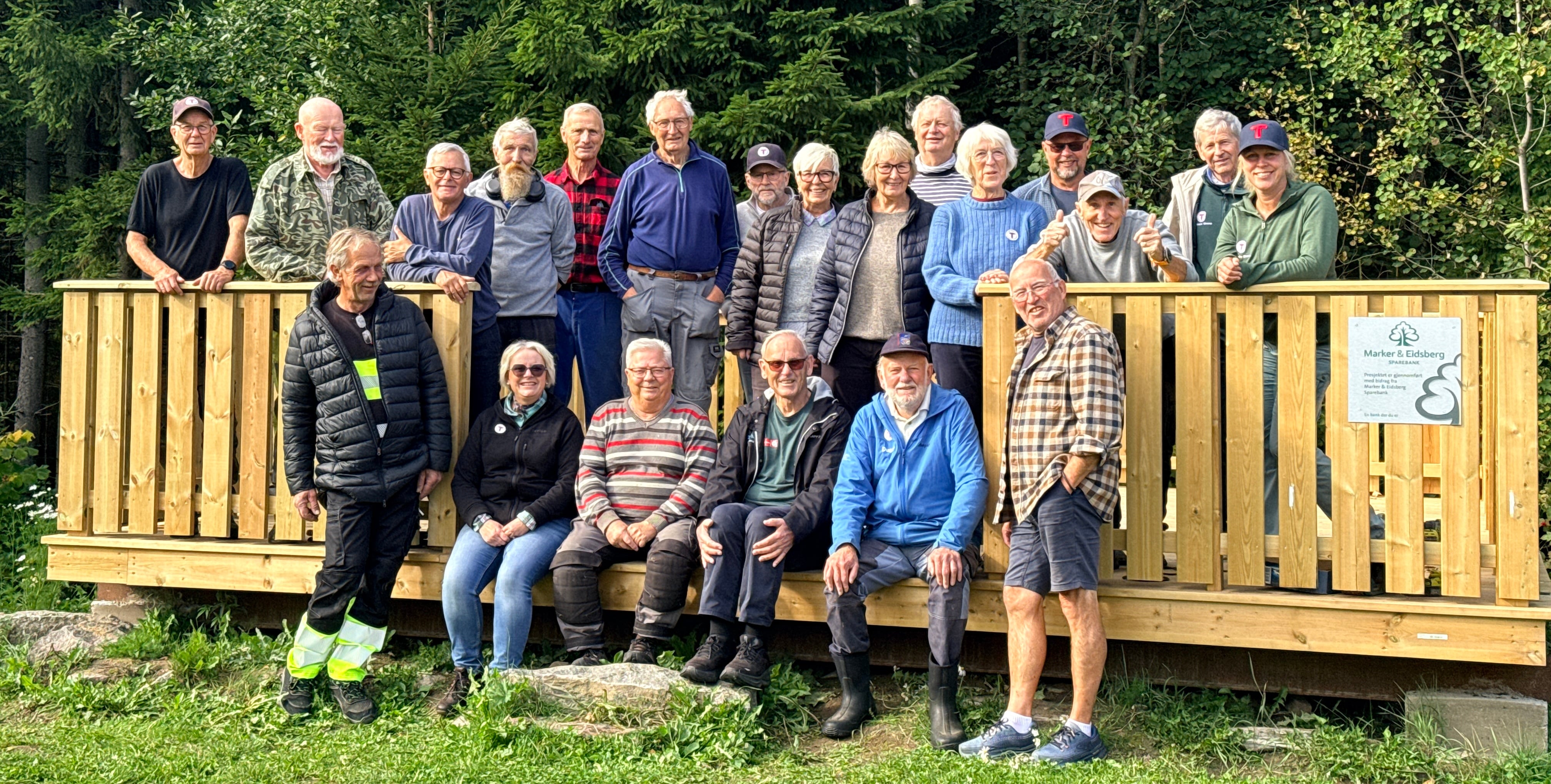 Bilde av en gjeng med mennesker stående på en platting. Skog i bakgrunnen.