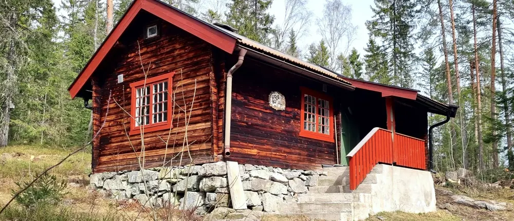 Gammel tømmerkoie med røde karmer og steinlagt grunnmur
