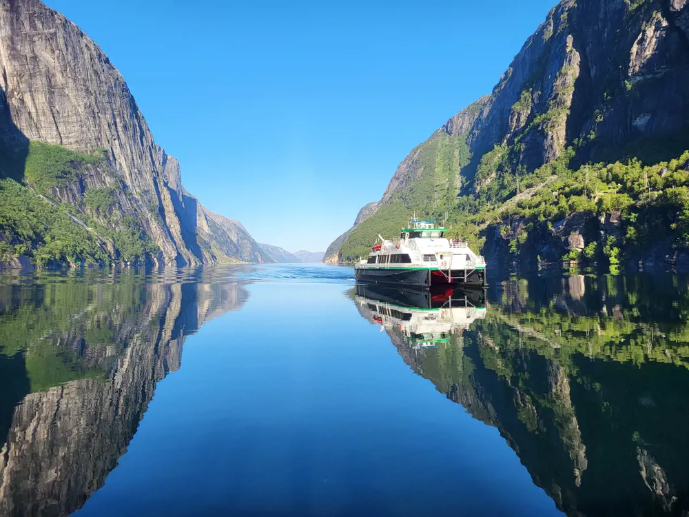 Bilde av en rutebåt som er på vei innover i Lysefjorden. Speilblank fjord med høye fjellsider.
