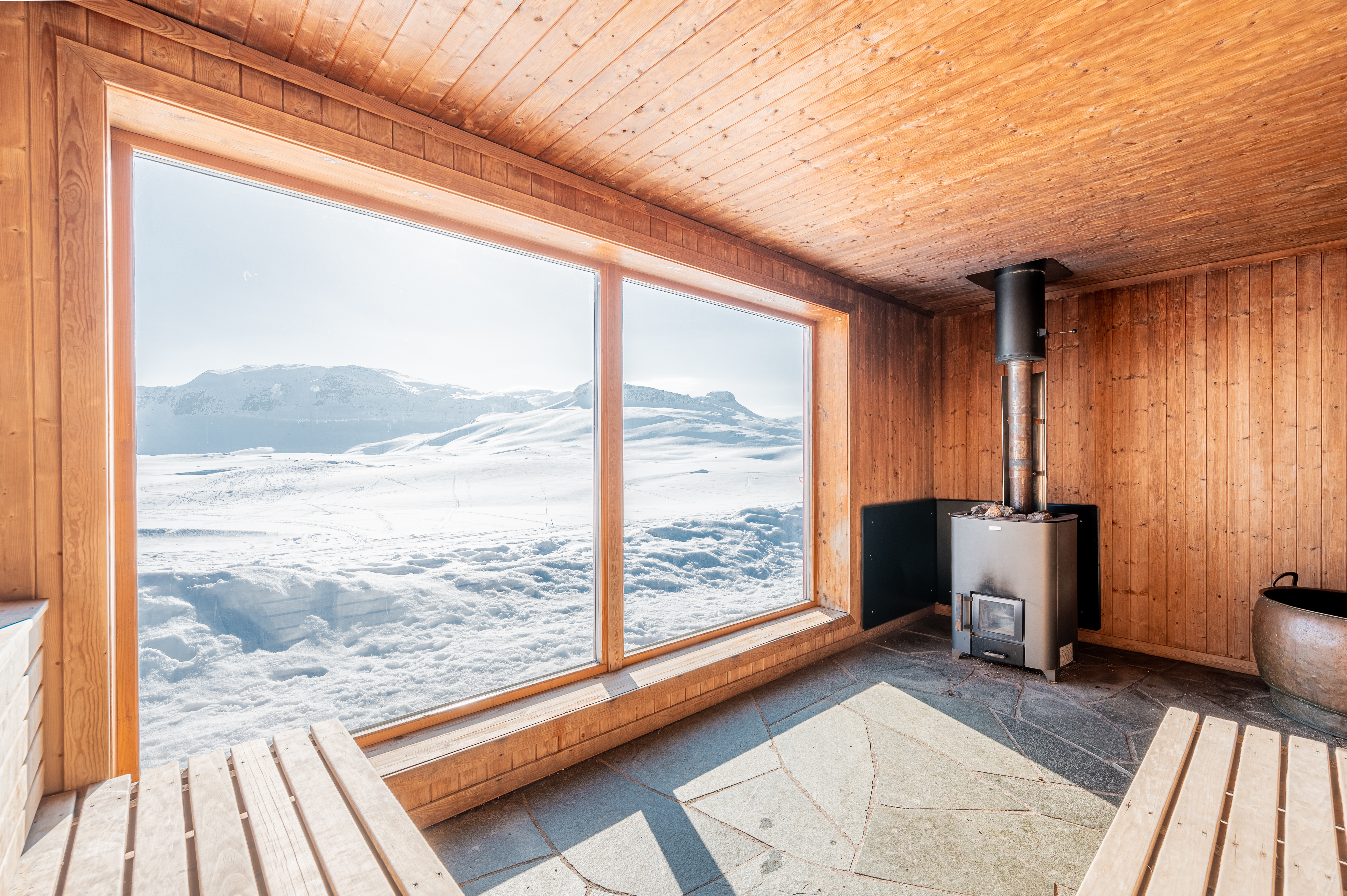 Foto. Badstue med store vinduer ut mot et vinterkledd fjellandskap