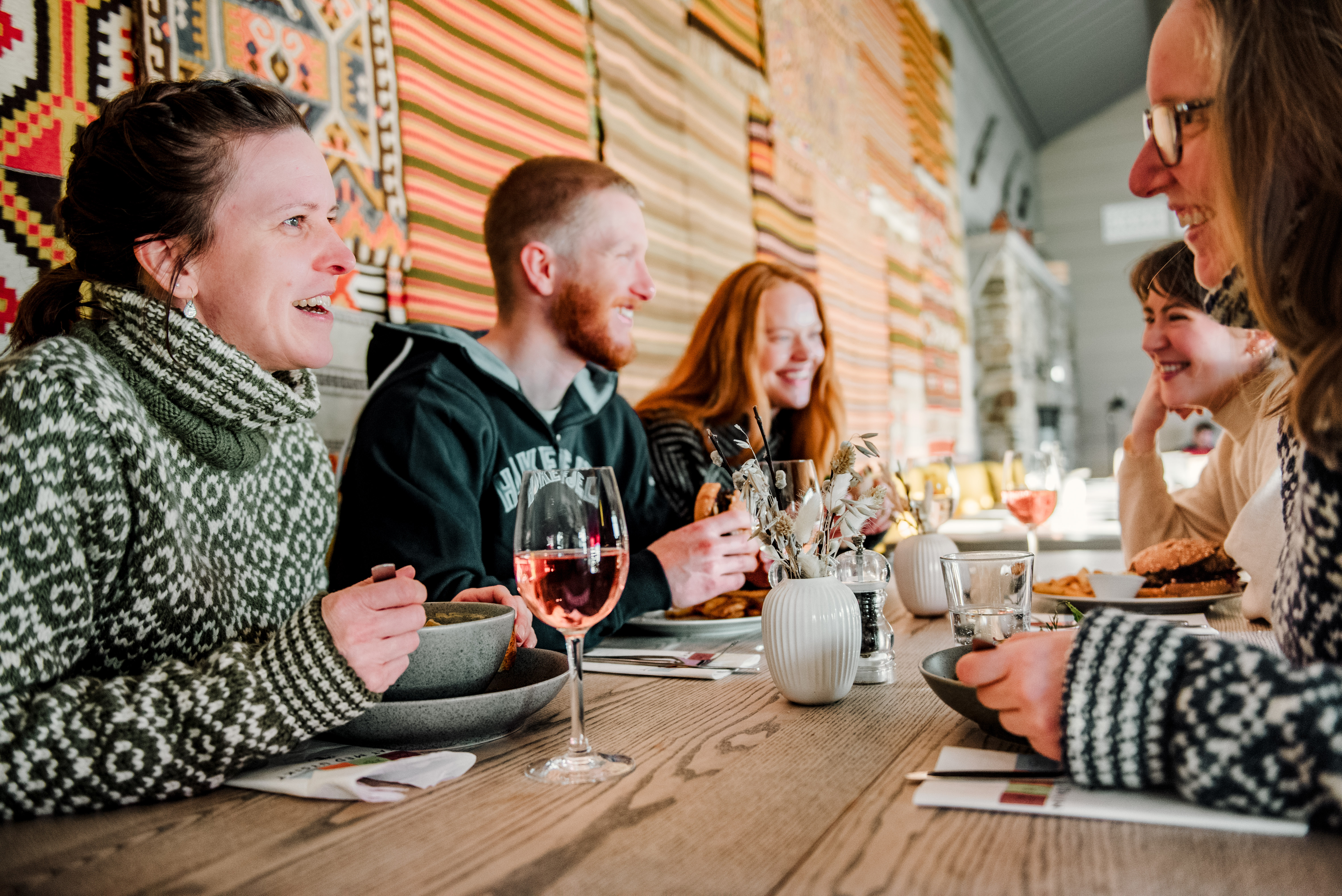 Foto. Fem personer sitter smilende rundt et bord og spiser. &Aring;kler i bakgrunnen