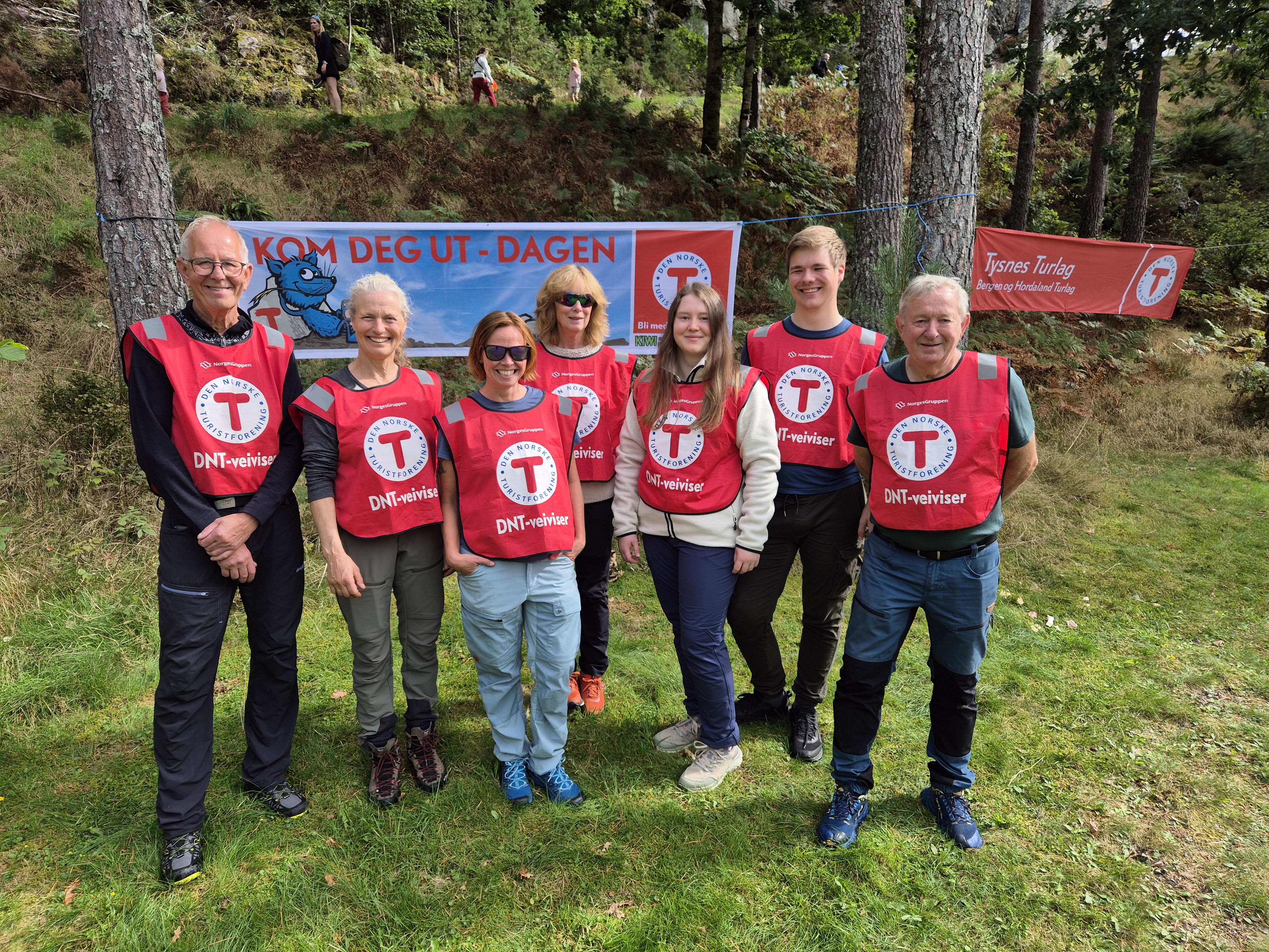 Gruppe mennesker st&aring;r i skog med r&oslash;d vest p&aring; seg.