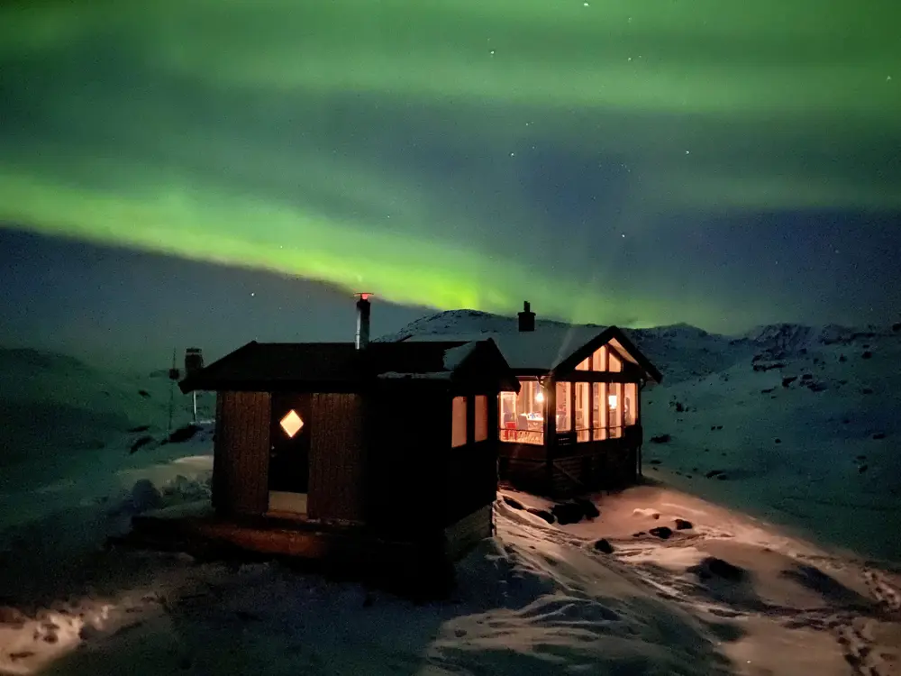 Hytte på snødekt fell opplyst av nordlyset