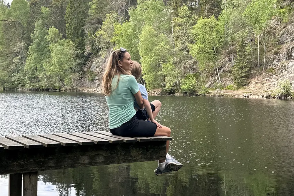 en mor og et barn på en bryggekant ved et skogsvann