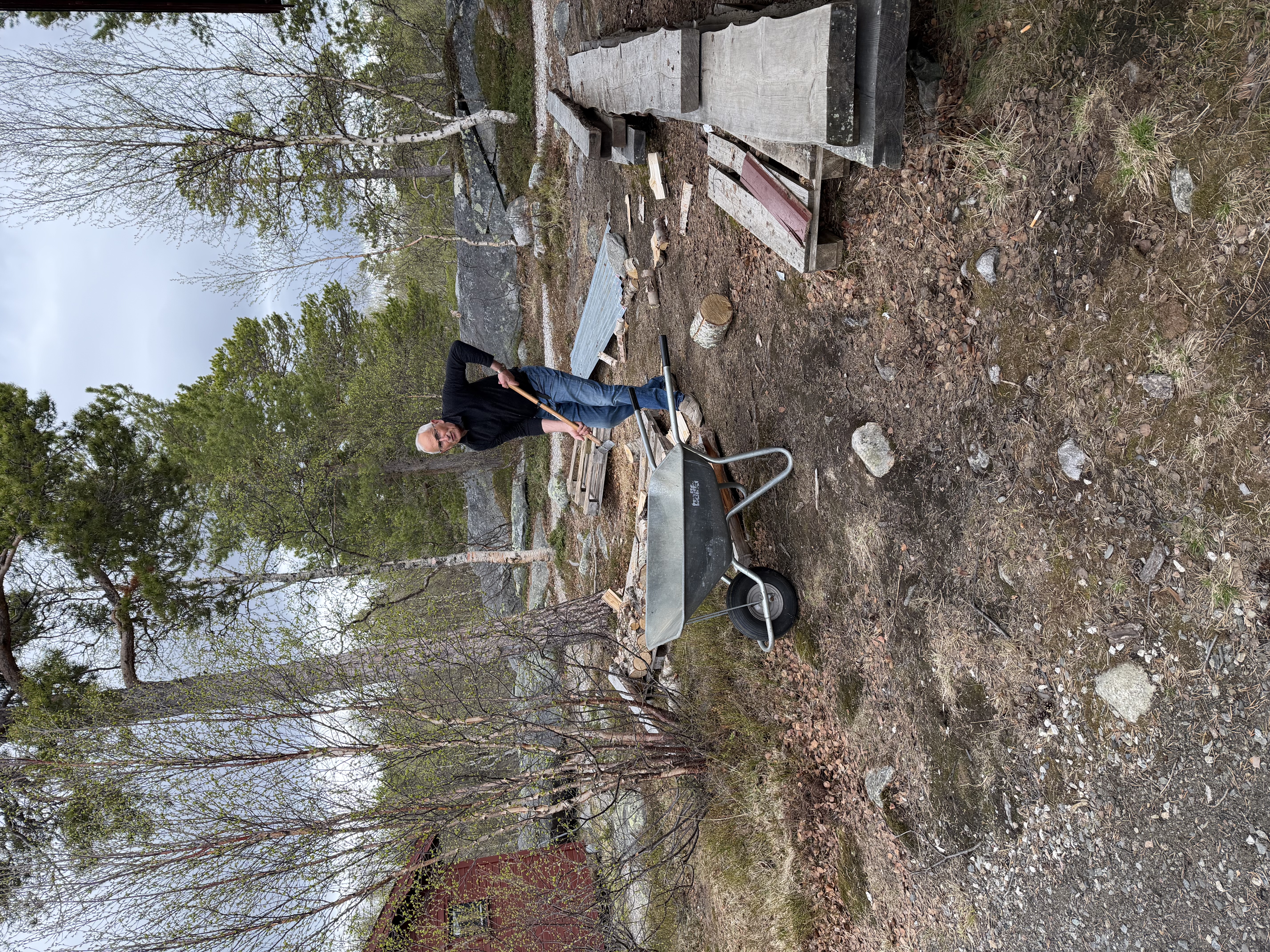 Mann som klyver ved. Trilleb&aring;r og kloppematerialer i forkant.
