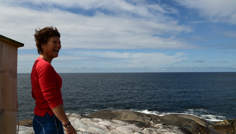 Person i rød genser står på et svaberg ut mot havet.