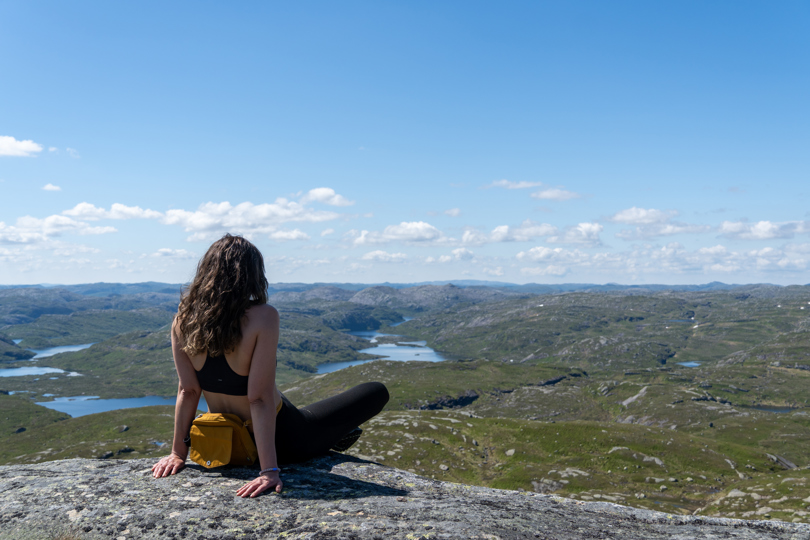 Kvinne sitter med ryggen til med utsikt mot fjellandskap bak.