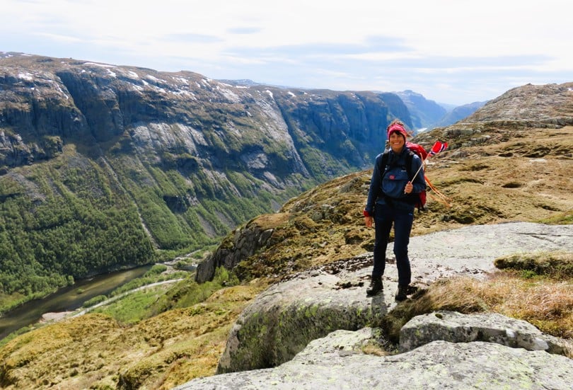 En dame står på en fjelltopp og holder et norsk flagg i hånden