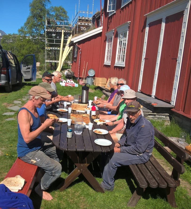 En dugnadsgjeng sitter rundt et bord ute i godværet og har et måltid sammen