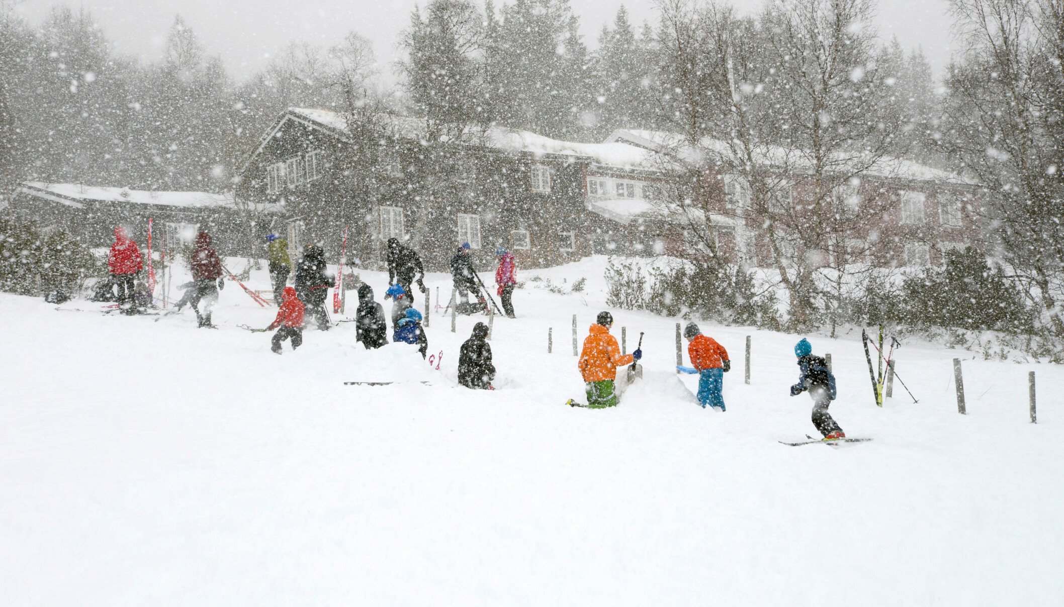 Mange barn aker og leker i snøvær utenfor ei turisthytte.
