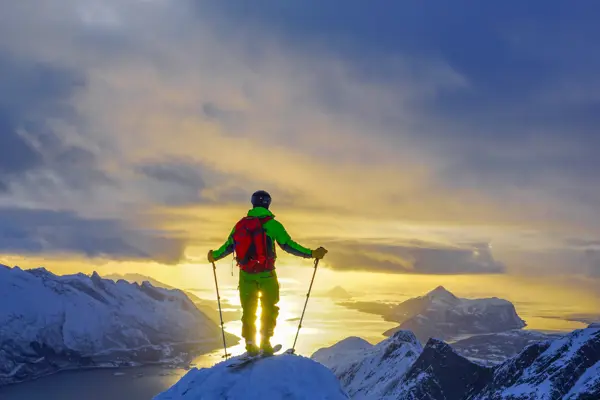 Person på ski på en fjelltopp med utsikt mot sola