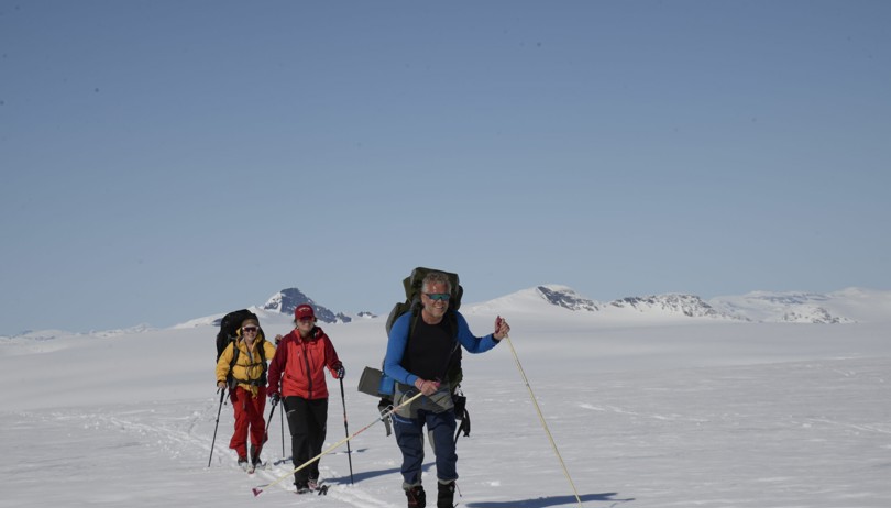 Tre personer går på ski over ei hvit vidde på fjellet.