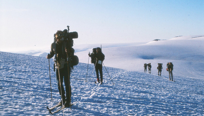 Gammelt bilde av flere personer som går på ski i over en bre.