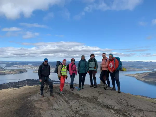 Gruppe mennesker på fjelltopp med utsikt mot fjorden bak.