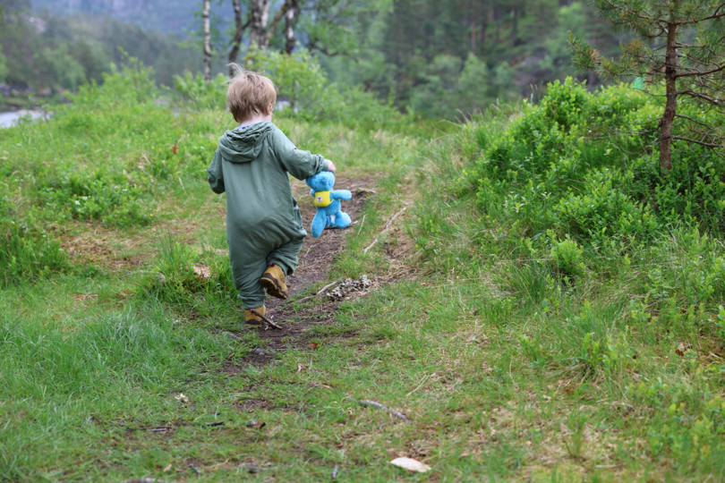 Gutt med bamse går på sti, sett bakfra.