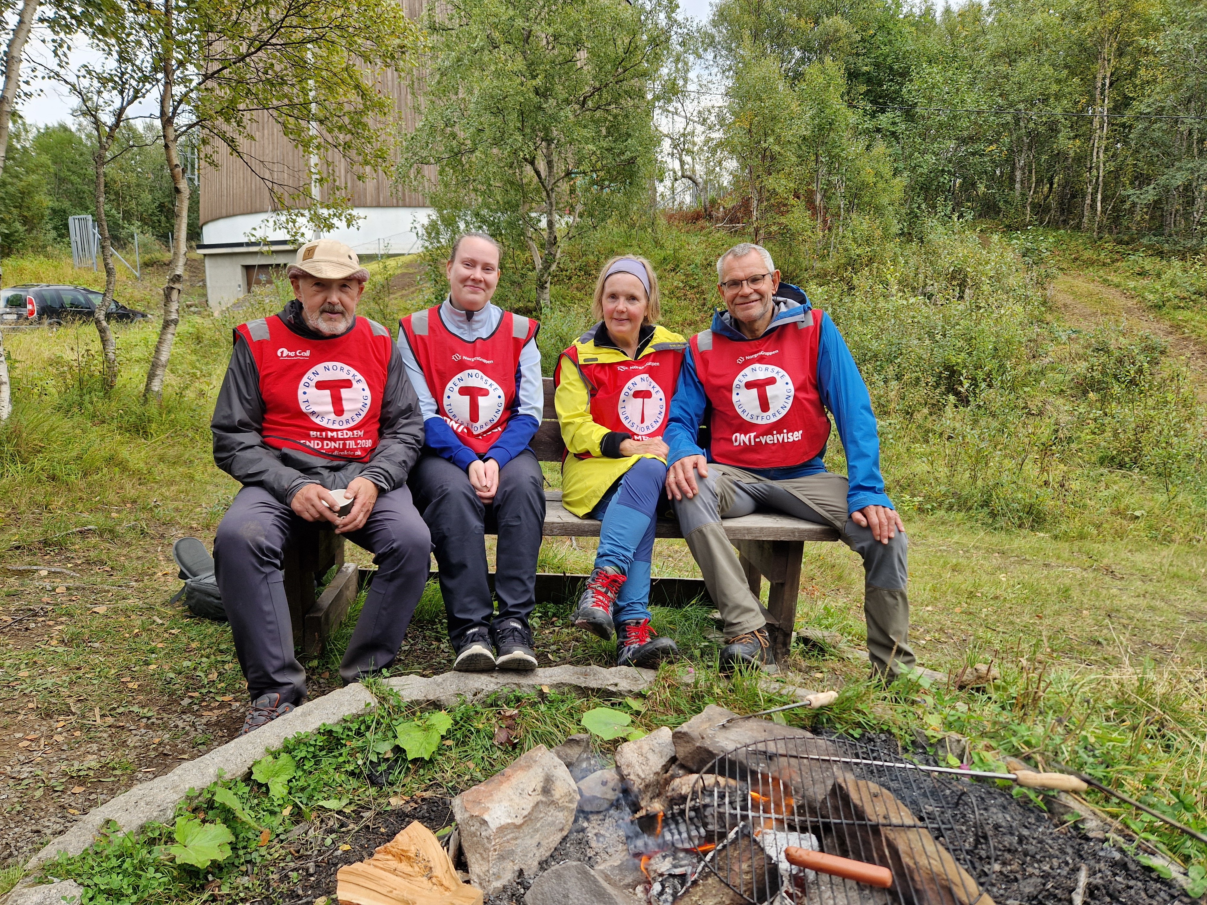 Fire frivillige med dnt-vest p&aring; en benk i skogen.