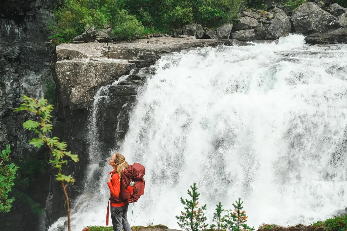 jente står foran en stor foss og nyter naturens lyder
