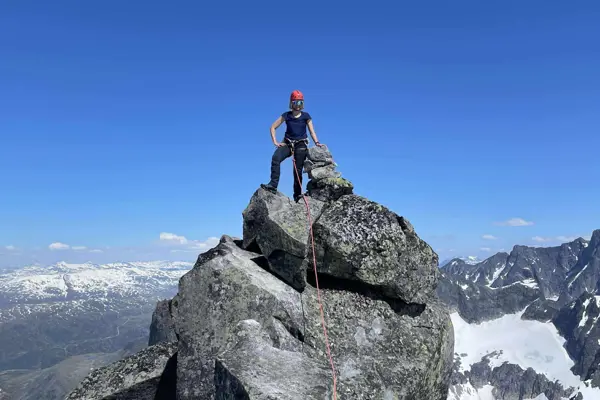 Kvinne står på toppen av fjell med utsikt mot snaufjell bak.