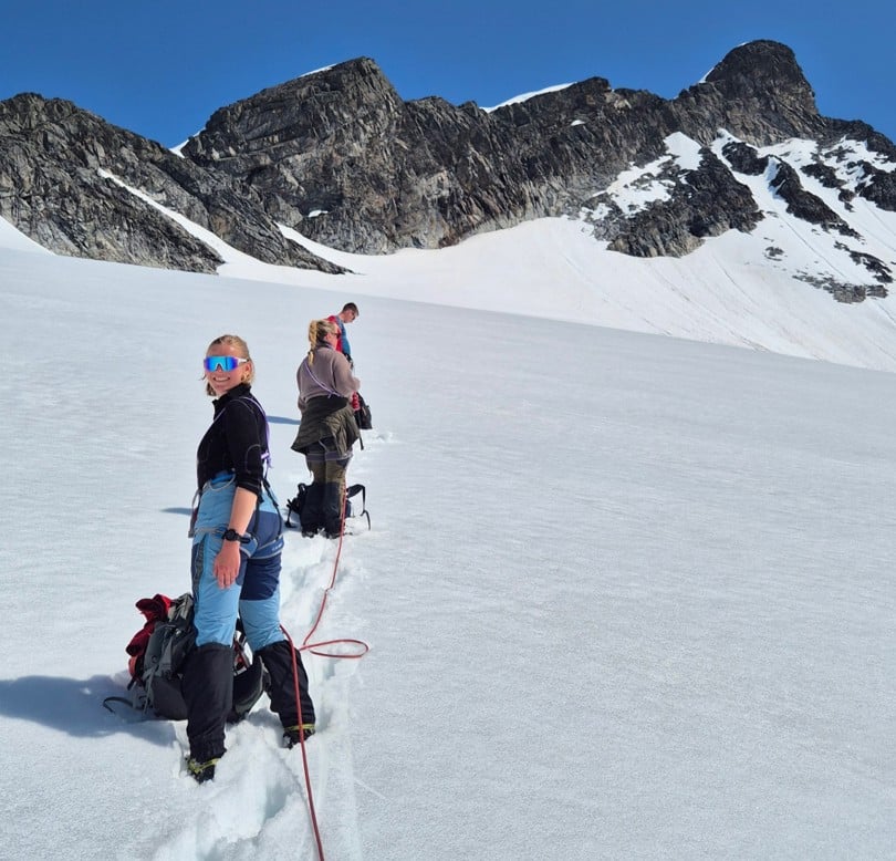 Kvinne står på bre og ser mot kamera med fjelltopp i bakgrunnen