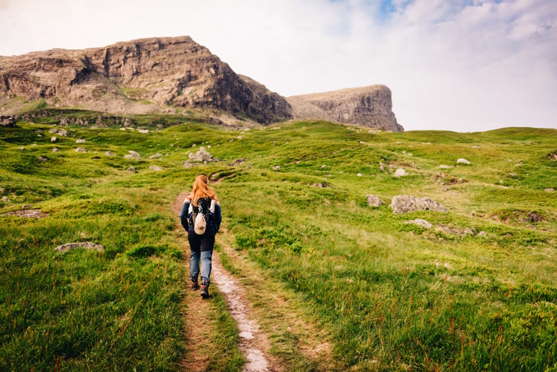 En Jente med rødt hår som går på tur i et frodig landskap med høye fjell i bakgrunnen
