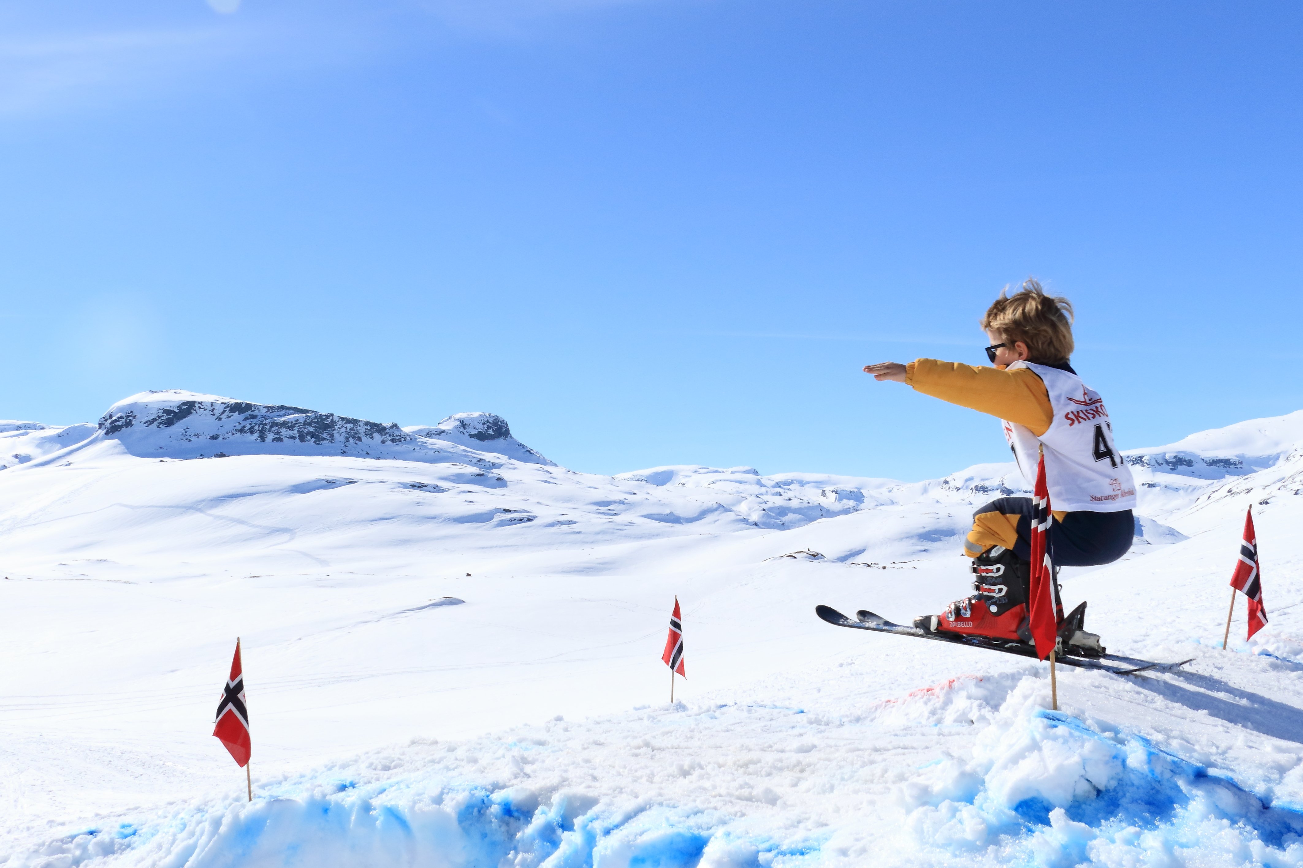 Et barn hopper p&aring; ski, bl&aring; himmle og fjell i bakgrunnen