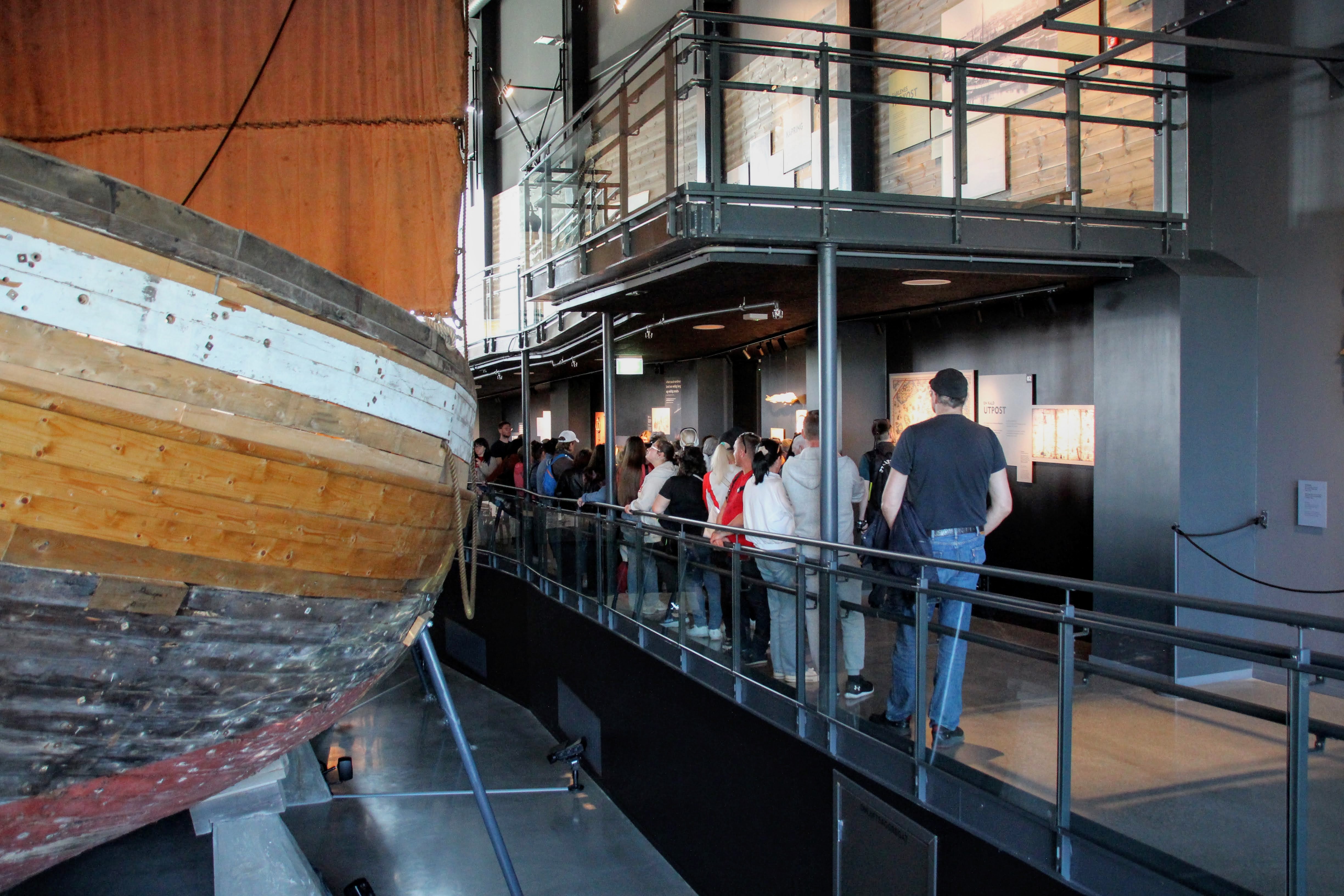 En gruppe mennesker står i kø ved siden av en stor jekt (båt) inne på et museum.