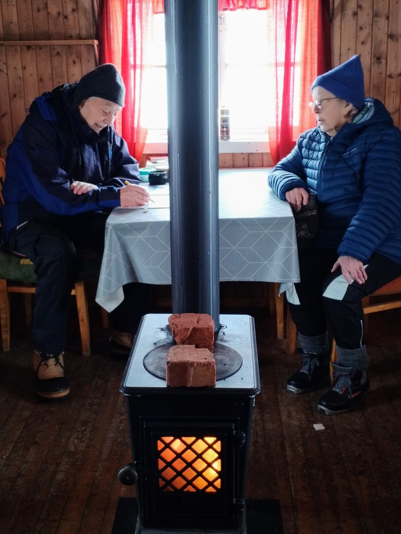 Mann og dame sitter inne i koia ved vedovnen.