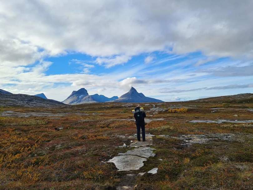 Jente som går med sekk foran fjellrekke