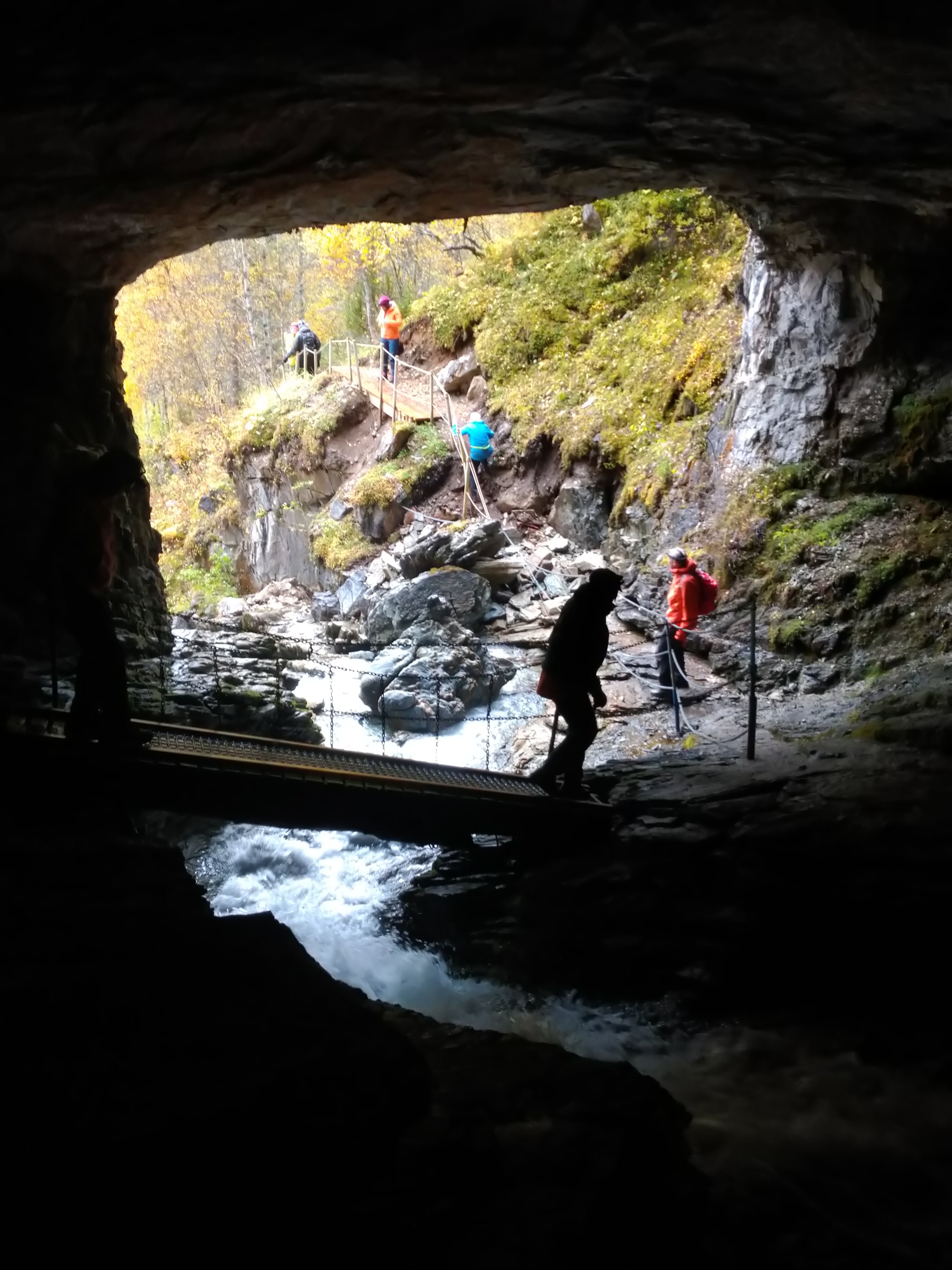 Grotte med bro som personer g&aring;r over med en foss under.