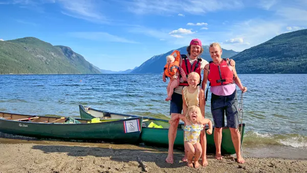 Mann, dame og tre barn foran en kano som ligger ved vannkanten med fjell i bakgrunnen