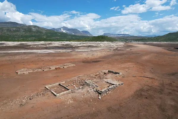 Et dronebilde tatt ovenfra, av den brune og gjørmete bunnen av en innsjø som er tappet ut, hvor ruinene av en grunnmur er synlig. 