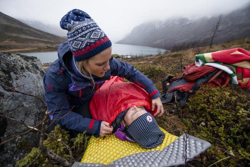 Kvinne legger vindsekk over dame som ligger på liggeunderlag i fjellet.