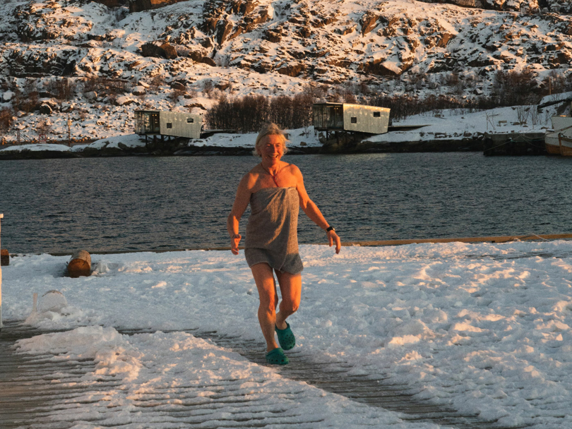 Person med grått håndkle går over en snødekt brygge etter et bad i sjøen. 