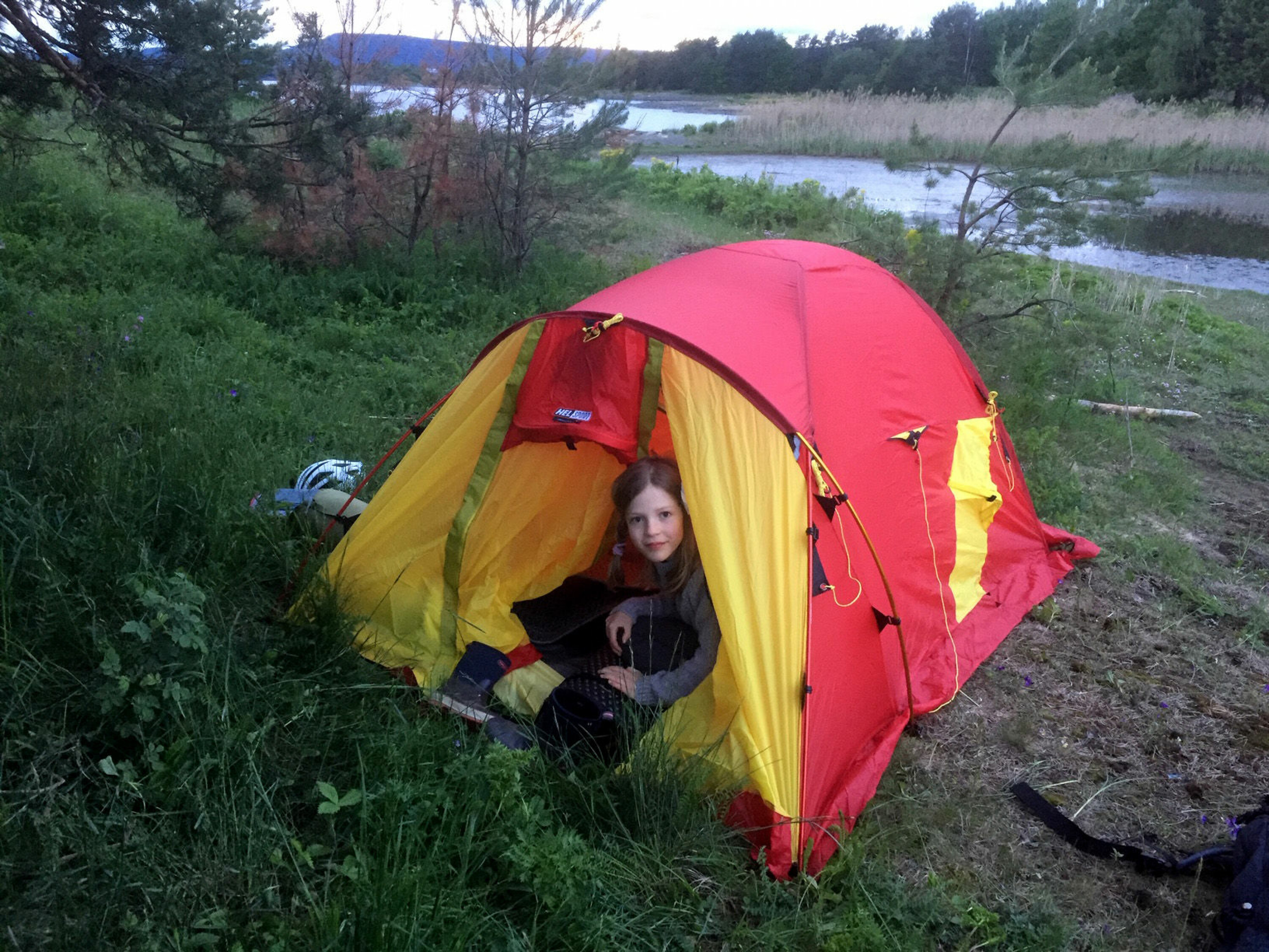 Jente stikker hodet ut av teltåpningen på et rødt og gult telt.