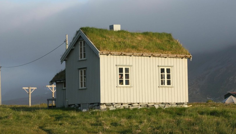 Lite og grått hus med torvtak. Rundt huset er det gresstuster.